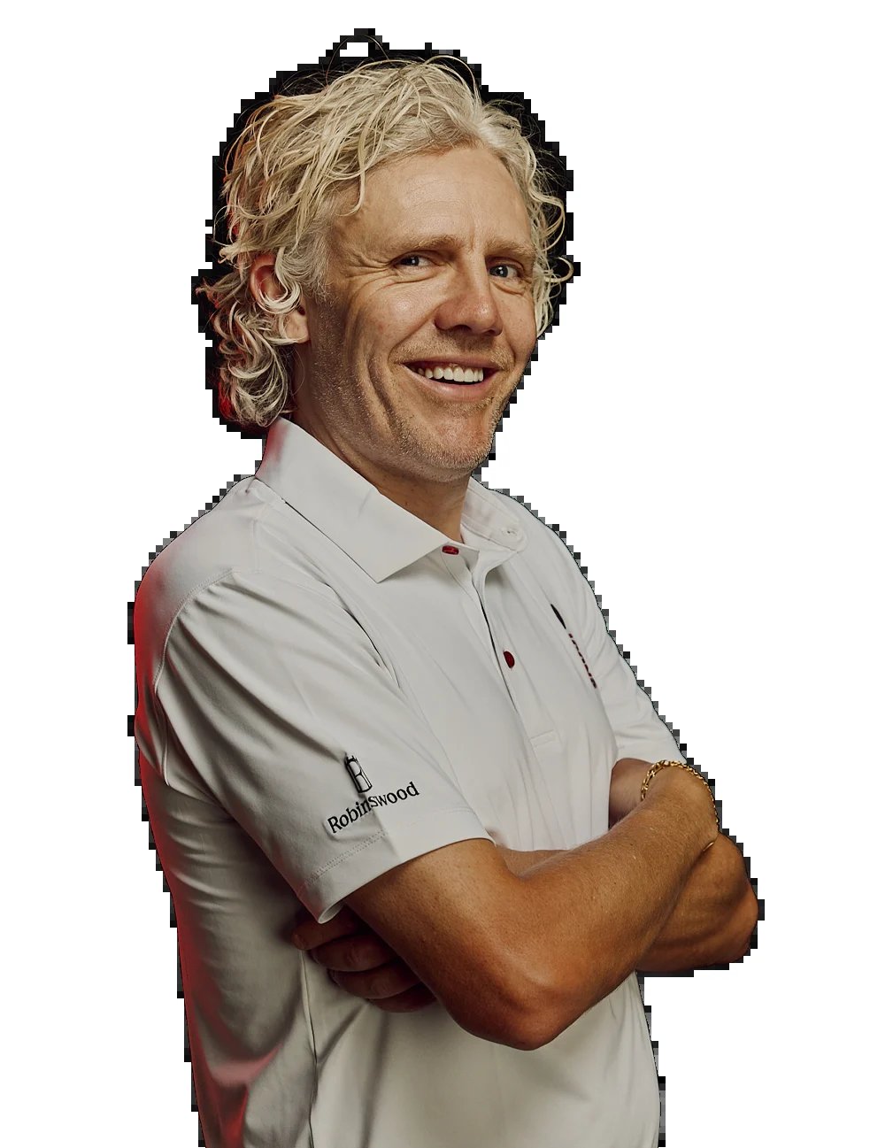 Man with blonde curly hair wearing white polo shirt smiling at camera with arms crossed against black background